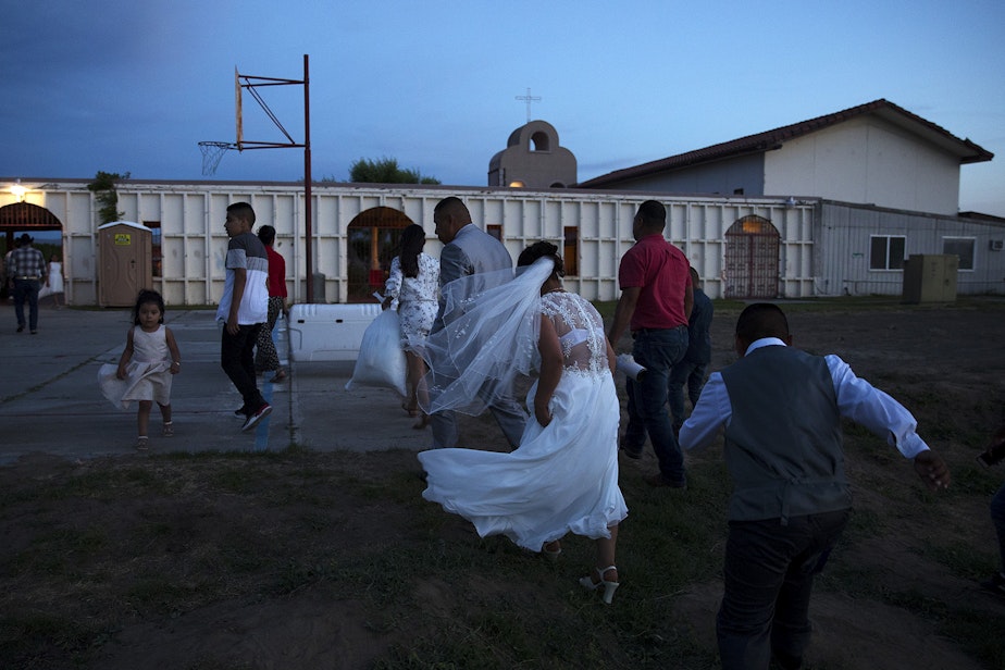 caption: Rosio Lopez leaves the mass wedding ceremony with her newlywed husband Alejandro Cruz at the end of the night after they were married along with 22 other couples on Sunday, June 2, 2019, at Our Lady of the Desert Church in Mattawa.