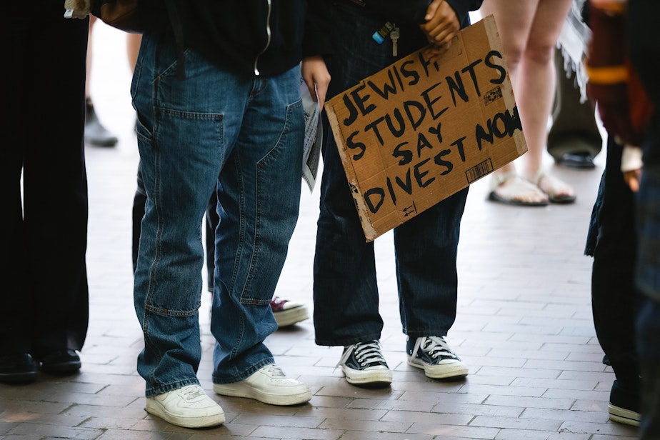 caption: ‘Jewish Students Say Divest Now,’ reads a sign as a crowd gathers for a rally outside of Gerberding Hall on behalf of students who were banned and suspended following an occupation of an engineering building, on Thursday, May 8, 2025, on the University of Washington campus in Seattle.