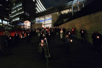 caption: Volunteers stand in silence for one hour on the steps of Seattle City Hall to honor those who died in 2021 on Tuesday, December 21, 2021.