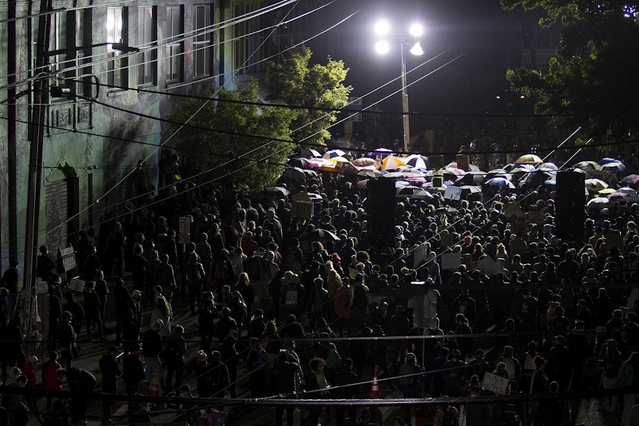caption: Hundreds of protesters are shown standing arm to arm before a fortified line of police officers in riot gear at 10:54 p.m. on Sunday, June 7, 2020, in Seattle.