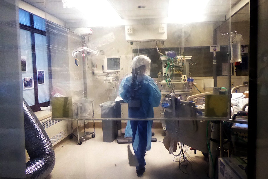caption: Leah Silver tends to her patient on the Covid ICU at the University of Washington Medical Center on April 24, 2020. There are photos of his family on the window.