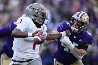 caption: Washington State quarterback Cameron Ward blocks Washington linebacker Carson Bruener as he runs with the ball during the first half of an NCAA college football game, Saturday, Nov. 25, 2023, in Seattle.