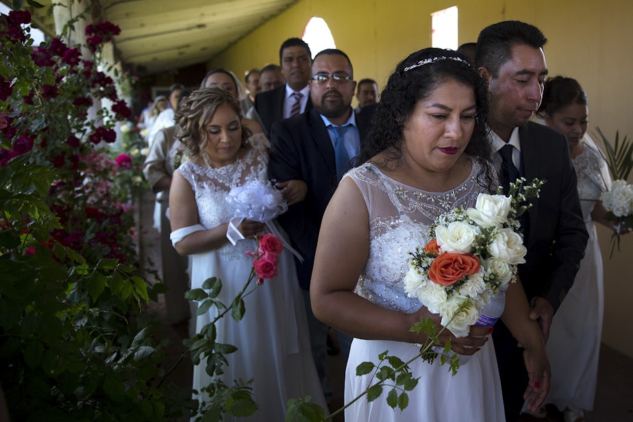 caption: Alma Mejia walks with her soon-to-be husband, Fortino Mejia, along with 22 other couples, to a mass wedding ceremony on Sunday, June 2, 2019, at Our Lady of the Desert Church in Mattawa.