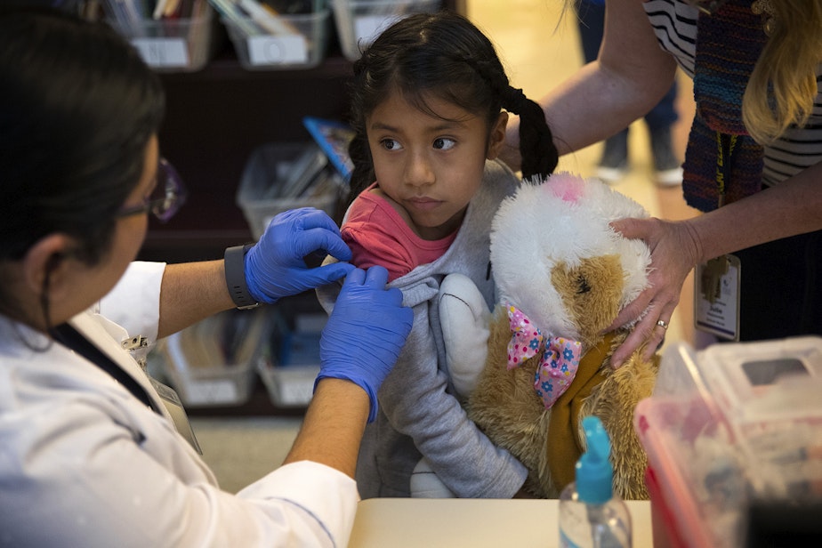 caption: Kindergartener Dariana Xilot Serrano looks at Erika Sandoval, a nurse with the Seattle Visiting Nurse Association, before receiving a flu shot on Tuesday, October 22, 2019, at Concord International Elementary School in Seattle.