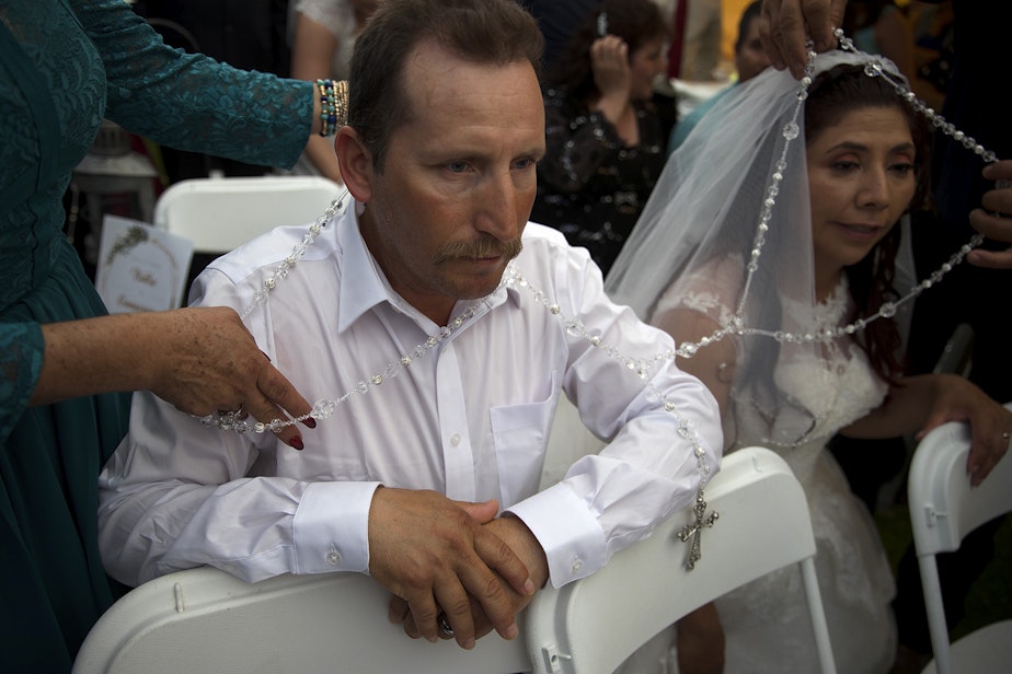 caption: A lasso de boda is placed around newlyweds Isidro Gómez and his wife Genoveva on Sunday, June 2, 2019, during a mass wedding ceremony where 23 couples were married at Our Lady of the Desert Church in Mattawa.