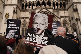 caption: A demonstrator holds a placard, after Stella Assange, wife of WikiLeaks founder Julian Assange, released a statement outside the Royal Courts of Justice, in London, Tuesday.