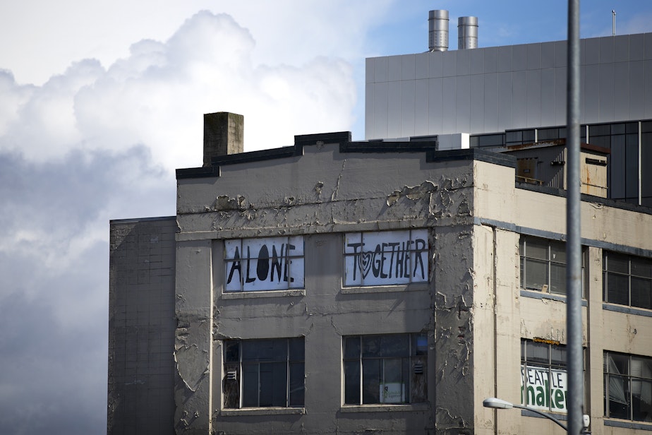 caption: 'Alone Together' reads a handwritten sign placed in the windows of a South Lake Union building, shown on Wednesday, March 25, 2020, in Seattle.