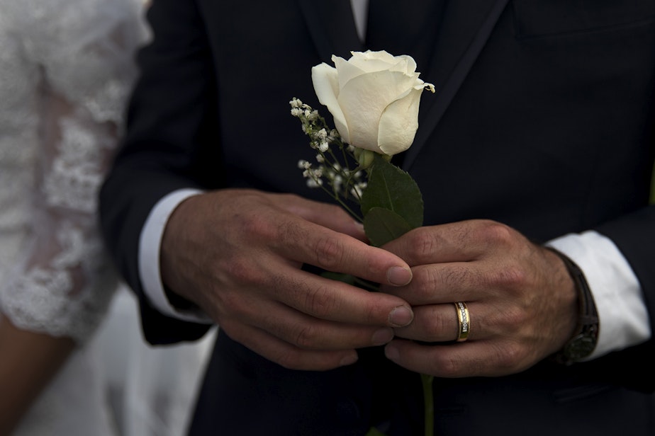caption: Himmbler Bernal holds a white rose while standing next to his wife, Lucelba, during a mass wedding ceremony on Sunday, June 2, 2019, at Our Lady of the Desert Church in Mattawa.
