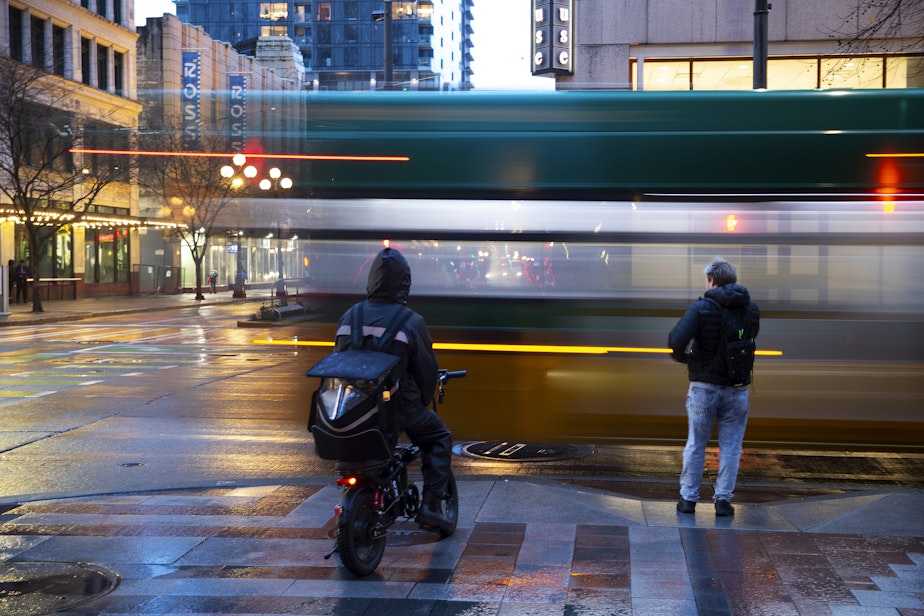 caption: Pedestrians wait to cross 4th Avenue as a King County Metro Bus speeds by, on Saturday, February 22, 2025, in downtown Seattle.