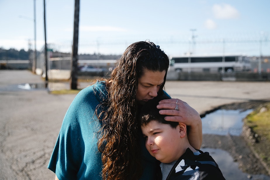 caption: Mary Loisate kisses the top of her 8-year-old son's head outside of the Northwest ICE Processing Center, where her husband is currently detained, on Monday, March 17, 2025, in Tacoma.