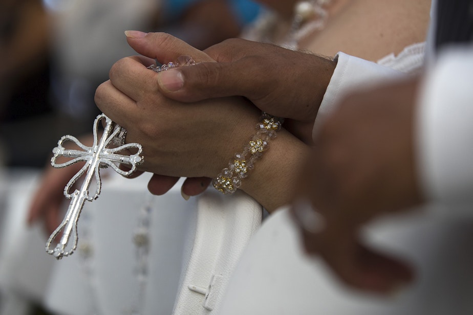 caption: Ana Dely Morales and Ramon Sanchez Cordova hold a lasso de boda together during a mass wedding ceremony where they were married along with 22 other couples on Sunday, June 2, 2019, at Our Lady of the Desert Church in Mattawa.