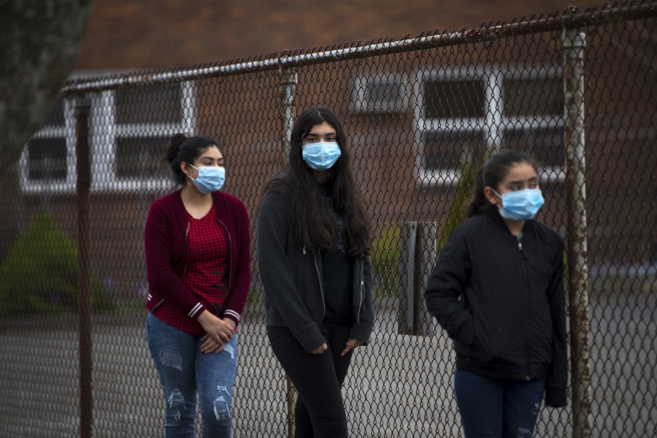 caption: From left, sisters Mia Hurtado, 14, Miliani Hurtado, 12, and Marleni Hurtado, 10, wait in line for walk and drive through confessions with Father Jose Alvarez on Friday, April 24, 2020, in the parking lot at Holy Roman Catholic Church in White Center.