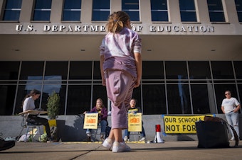 caption: Alejandra Rodriguez, 9, of Key Largo, Fla., watches as college students protest in support of the Department of Education, Thursday, March 20, 2025, outside the department in Washington.