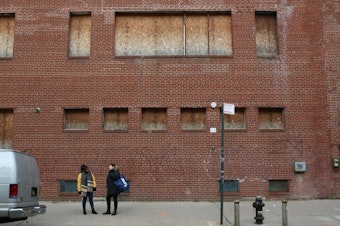 caption: Lena Afridi and Sabrina Jalal stand before a boarded up Queens building on property Amazon will occupy.