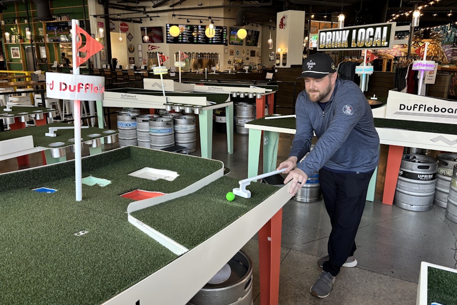 caption: Ryan Anderson is general manager at Flatstick Pub in Redmond, across the street from the light rail station. He demonstrates the pub's trademarked pub game, Duffleboard.