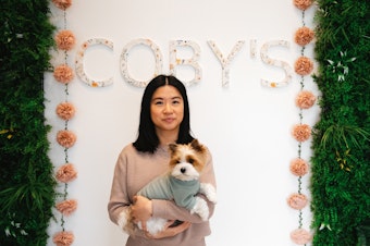 caption: Mary Wu, owner of Coby’s Cafe is portrayed holding her dog, Coby, on Tuesday, April 1, 2025, at the dog cafe in Seattle. 