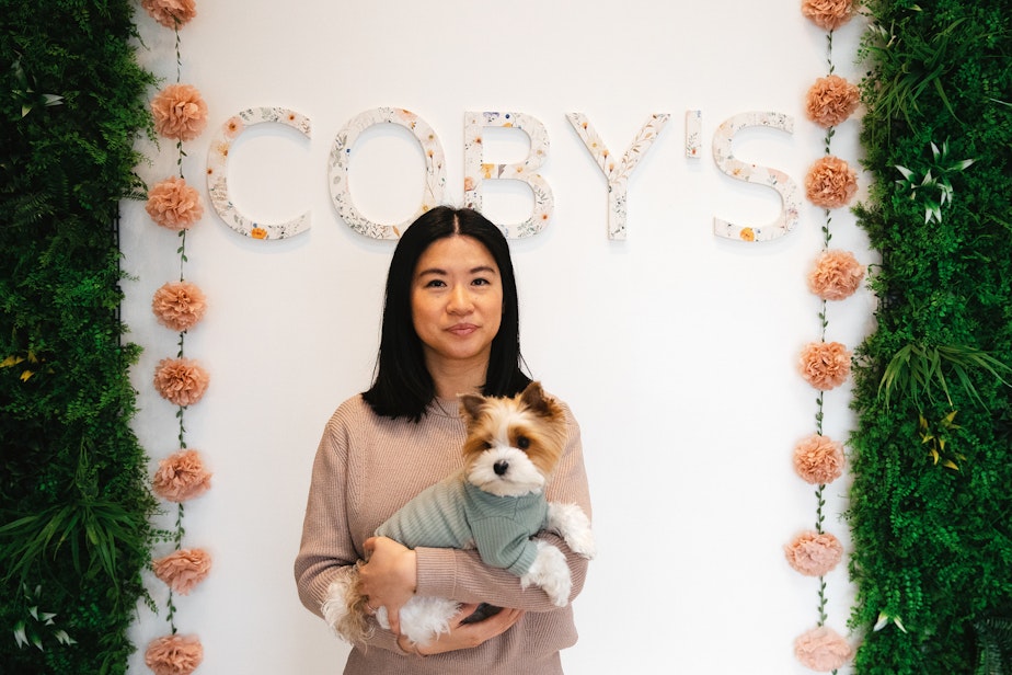 caption: Mary Wu, owner of Coby’s Cafe is portrayed holding her dog, Coby, on Tuesday, April 1, 2025, at the dog cafe in Seattle.