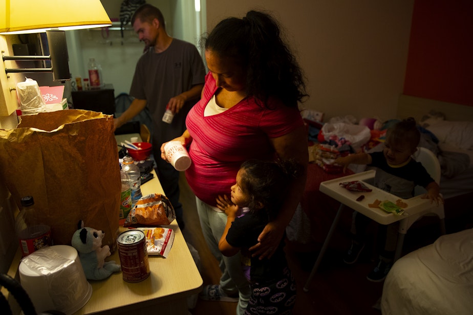 caption: Tynikki Arnold and Sean prepare ramen noodles for dinner for Vay, 5, and Messiah, 1, in their room at a Motel 6, on Friday, August 26, 2022. The family is staying at the motel after a fire tore through their apartment complex.