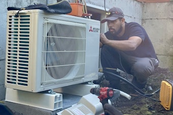 caption: CM Heating technician Saul Benitez installs an electric heat pump in Shoreline, Washington, on July 28, 2023.