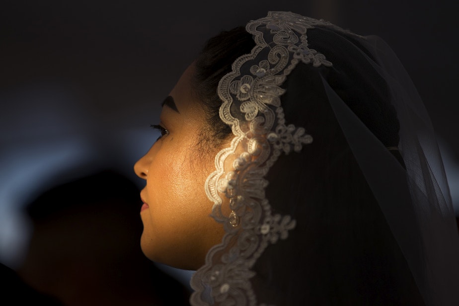 caption: Light shines on Janeli Alcala's face during a mass wedding ceremony for 23 couples on Sunday, June 2, 2019, at Our Lady of the Desert Church in Mattawa.