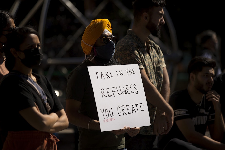 caption: Angad Singh holds a sign that reads, 'Take in the refugees you create,' while attending a rally and march in solidarity with Afghans on Saturday, August 28, 2021, at Westlake Park in Seattle.
