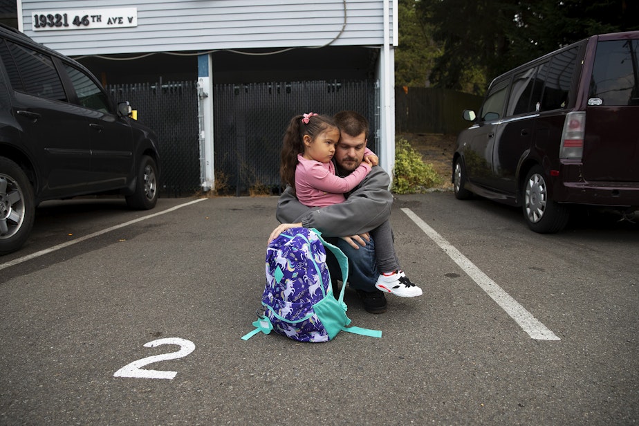caption: Sean holds Vay, 5, as they wait for the school bus on the first day of school on Monday, September 12, 2022, outside of their apartment complex in Lynnwood.