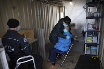 caption: Jennifer, who preferred to go by her first name only, hugs her mother, Du, 87, after she received her first dose of the Moderna Covid-19 vaccine, administered by Seattle Firefighter and EMT Dave Pedras, left, on Thursday, February 18, 2021, during a pop-up vaccination clinic at the West Seattle Covid-19 testing site on Southwest Thistle Street in Seattle.