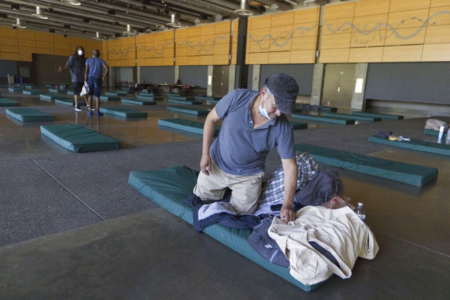 caption: Roberto Cedomio prepares his bed at a cooling shelter run by the Salvation Army at the Seattle Center during a heat wave hitting the Pacific Northwest on June 27, 2021. Seattle set a record high for the day. Cedomio said he was glad to have this place available in the heat.