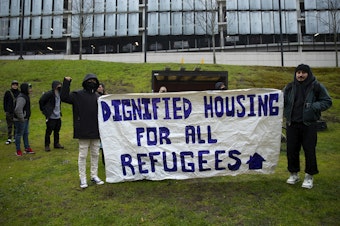 caption: "Dignified Housing for All Refugees" reads a banner as asylum seekers once housed at the Sleep Inn in SeaTac march to Seattle City Hall along with activists, mutual aid organizations and allies to ask for assistance with housing from the Seattle City Council on Tuesday, February 27, 2024, in Seattle. 