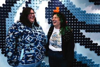 caption: Ashley Hufford, left, and Gina Rome, right, laugh together while being portrayed in front of the ‘puck wall’ on Tuesday, April 29, 2025, at the Kraken Community Iceplex in Seattle. 