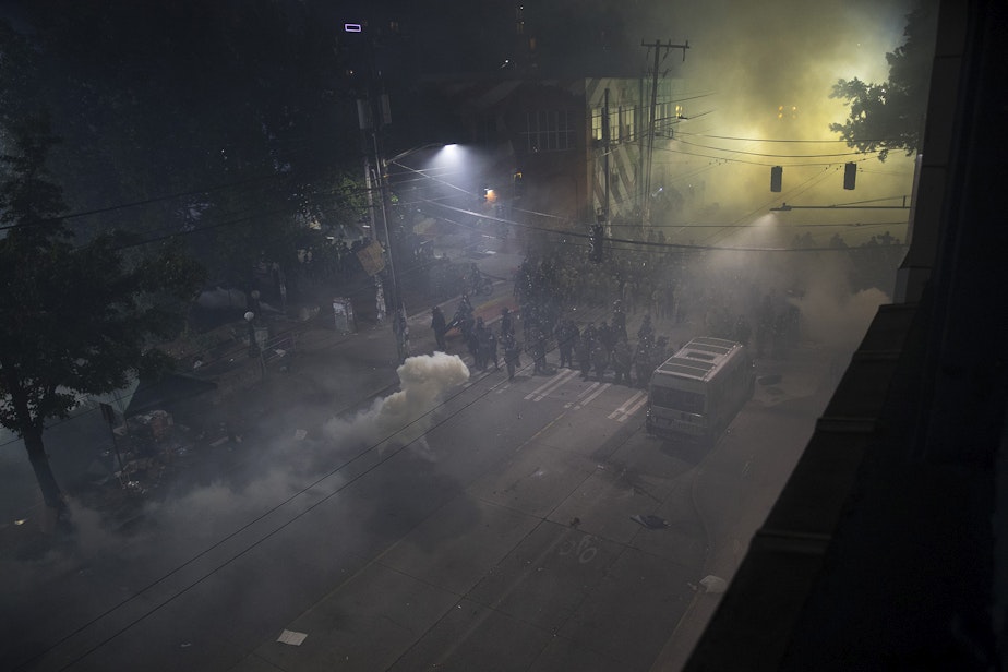 caption: Seattle police officers are shown shrouded in tear gas at the intersection of East Pine Street and 11th Avenue at 12:12 a.m. on Monday, June 8, 2020, in Seattle.