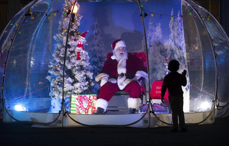 caption: Seattle Santa Dan Kemmis talks with 4-year-old Otto on Sunday, December 6, 2020, from inside a snow globe at the intersection of Greenwood Avenue North and North 76th Street in Seattle.