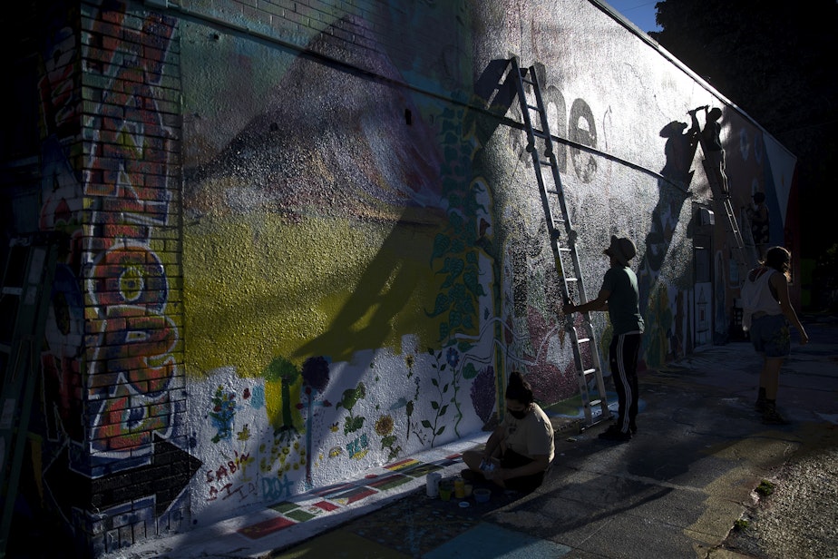 caption: Muralist Carlos Nieto-Mosqueda, right, works on a neighborhood mural project at the intersection of Beacon Avenue South and South Hanford Street on Monday, July 20, 2020, in Seattle. "It only makes sense for color to brighten up a neighborhood," said chef Tarik Abdullah.