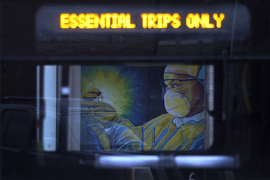 caption: A mural of a health care worker is shown through a passing King County Metro bus on Tuesday, April 28, 2020, along South Main Street in Seattle.
