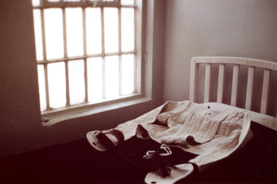caption: A photo of what appears to be a straitjacket lying on a bed by a window. The image was found in the files of Northern State Hospital at the Washington State Archives in Olympia.