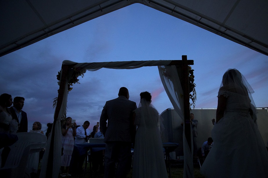 caption: Couples wait their turn to take a photograph with the wedding cake after a mass wedding ceremony on Sunday, June 2, 2019, at Our Lady of the Desert Church in Mattawa.