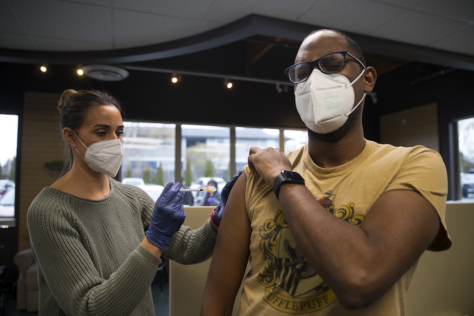 caption: Volunteer registered nurse Amy Rioux, left, administers a Covid-19 vaccine for Teddy Haile of Seattle, right, on Wednesday, April 7, 2021, at Island Drug in Oak Harbor.