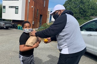 caption: Gerald  Donaldson, a family support worker at Leschi Elementary in Seattle, hands off some school lunches to third-grader Elijah Baker.