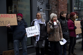 caption: Martha Baskin leads a chant with other members of the Troublemakers group while demonstrating in front of the Tesla showroom in South Lake Union, on Thursday, Feb. 13, 2025, in Seattle. 