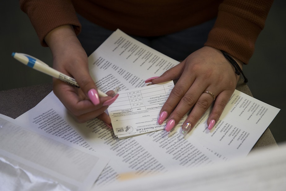 caption: Customer service representative Virginia Martinez adds the date to CDC vaccination record cards on Wednesday, April 7, 2021, at Island Drug in Oak Harbor.