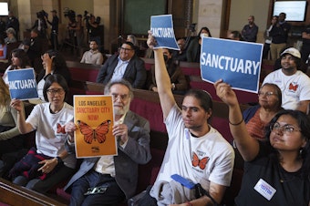 caption: Members of immigration advocacy groups react as Los Angeles City Council votes to enact an ordinance to prohibit city resources from being used for immigration enforcement in anticipation of potential mass deportations under President-elect Donald Trump, inside Los Angeles City Hall on Tuesday, Nov. 19, 2024. 