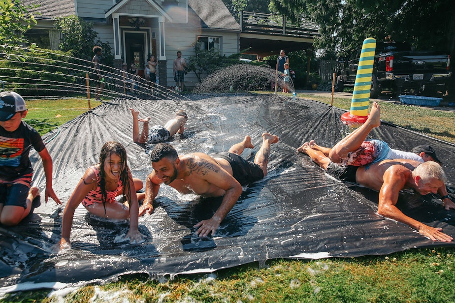 caption: Vasili Vouros, center, and John Cain Jr., right, slip n' slide with their kids in Vouros's front yard in Skyway.
