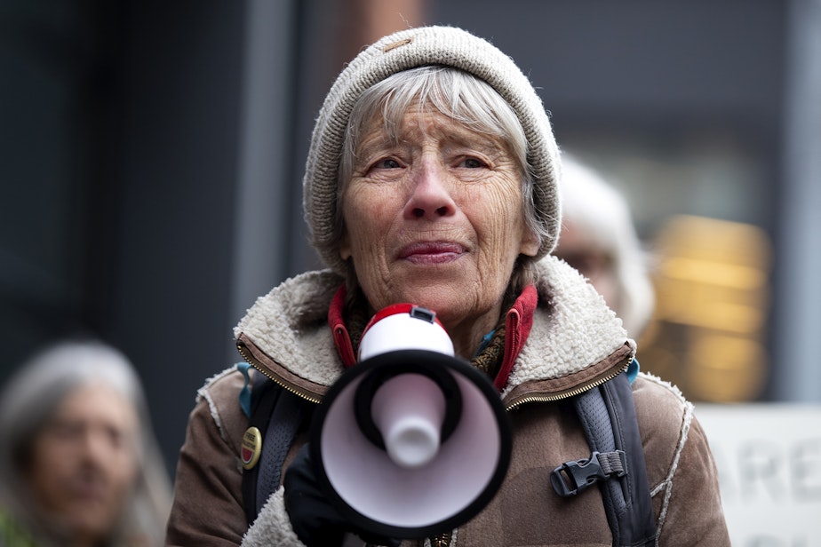 caption: Martha Baskin leads a chant with other members of the Troublemakers group while demonstrating in front of the Tesla showroom in South Lake Union, on Thursday, Feb. 13, 2025, in Seattle.
