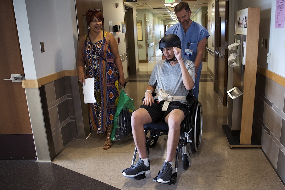 caption: LaDonna Horne smiles as her son, DaShawn Horne, raises his fist in the air in celebration as he leaves the hospital after 103 days with the help of his nurse Derek Bergey, on Thursday, May, 3, 2018, at Harborview Medical Center in Seattle.
