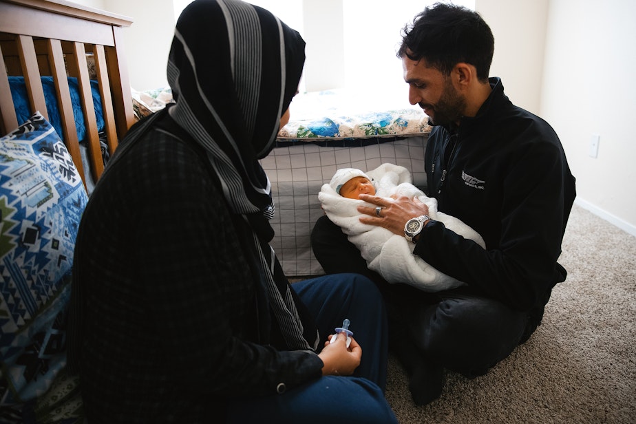 caption: Adela, left, and Jabar Mahmoudi, right, care for their one week old son, Omar, on Monday, March 31, 2025, at their family members apartment in Kent.