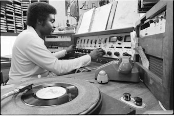 caption: DJ Robert L. Scott in booth at Black-owned KYAC radio station, Seattle, May 1975.