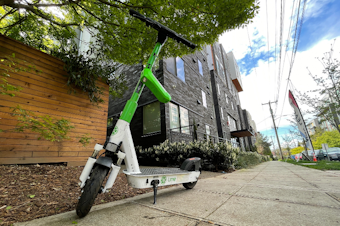 caption: A Lime scooter parked on a Northeast Seattle sidewalk. 