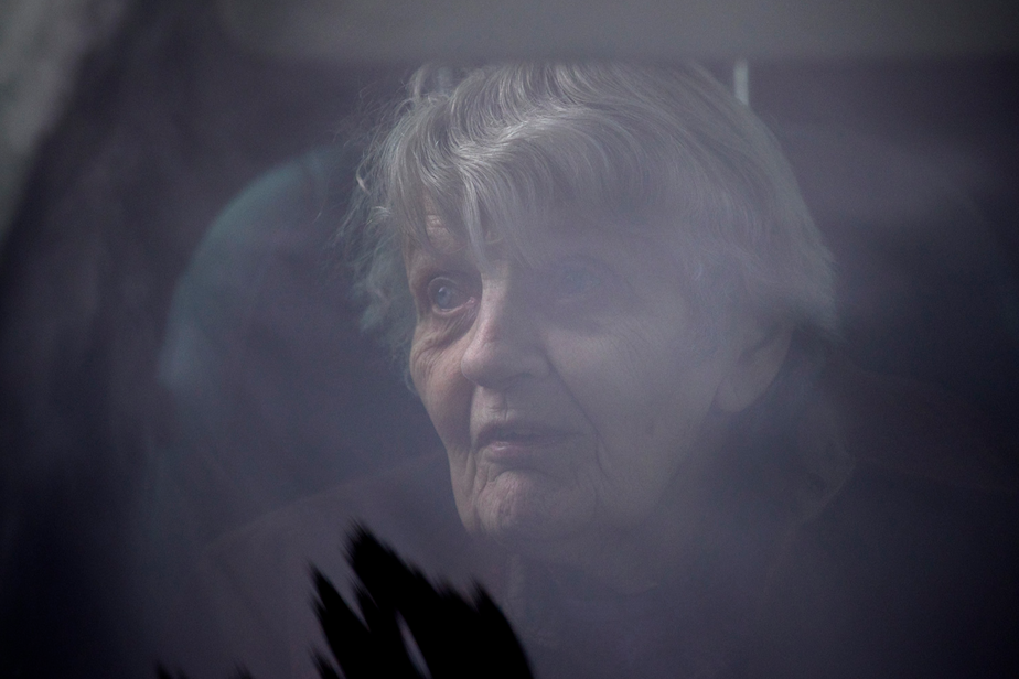 caption: Dorothy Campbell sits in her son, Charlie Campbell's vehicle, after knocking on her husband, Gene Campbell's window at Life Care Center of Kirkland and speaking to him through the phone, on Thursday, March 5, 2020, in Kirkland. Charlie Campbell came all the way from Silver City, New Mexico, to take his mother to see his father.